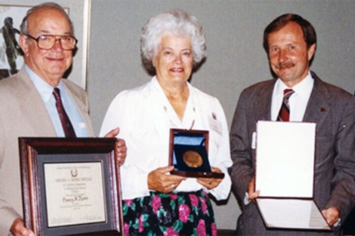 Dottie Rosso stands with two other people and holds an award.